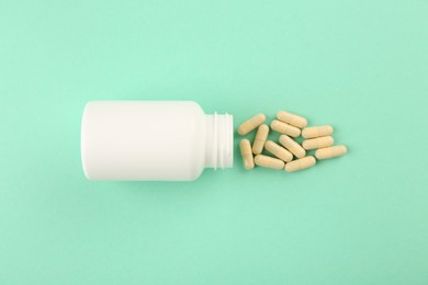 Bottle and vitamin capsules on turquoise background, top view