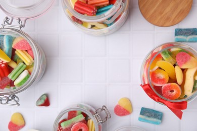 Photo of Frame made of glass jars with tasty colorful jelly candies on white tiled table, flat lay. Space for text