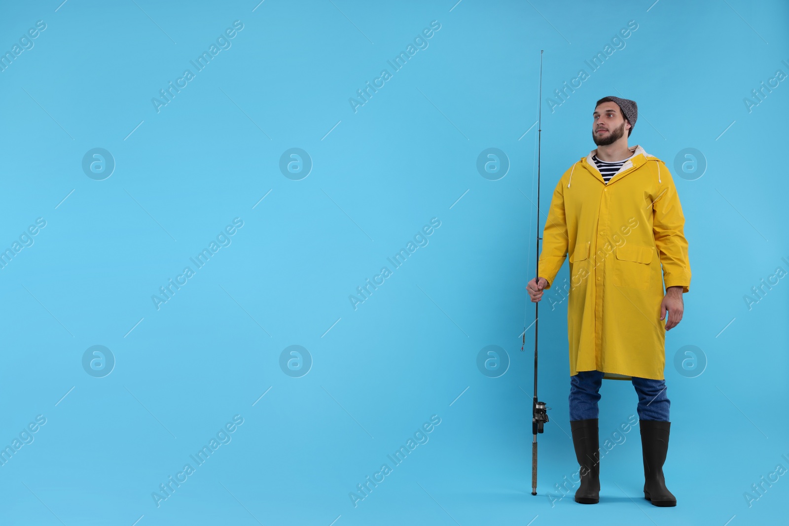 Photo of Fisherman with fishing rod on light blue background, space for text