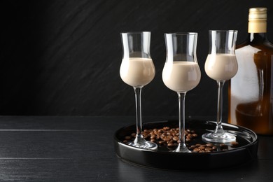 Coffee cream liqueur in glasses, bottle and beans on black wooden table, space for text