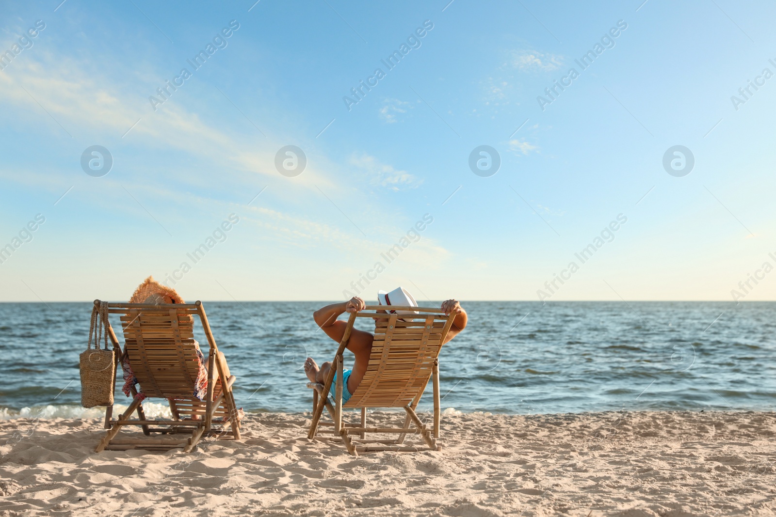 Photo of Young couple relaxing in deck chairs on beach near sea