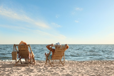 Photo of Young couple relaxing in deck chairs on beach near sea