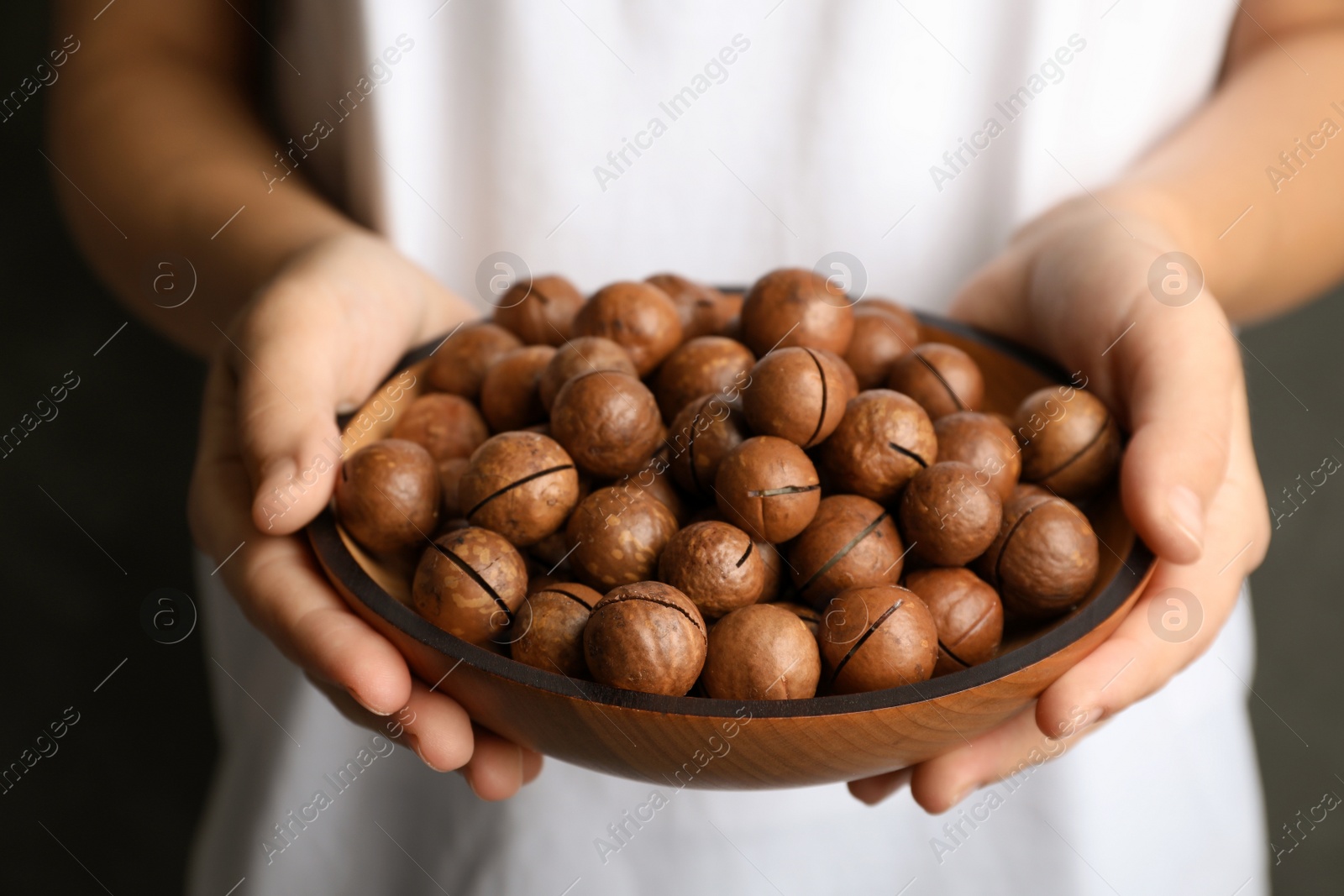 Photo of Woman holding plate with organic Macadamia nuts, closeup