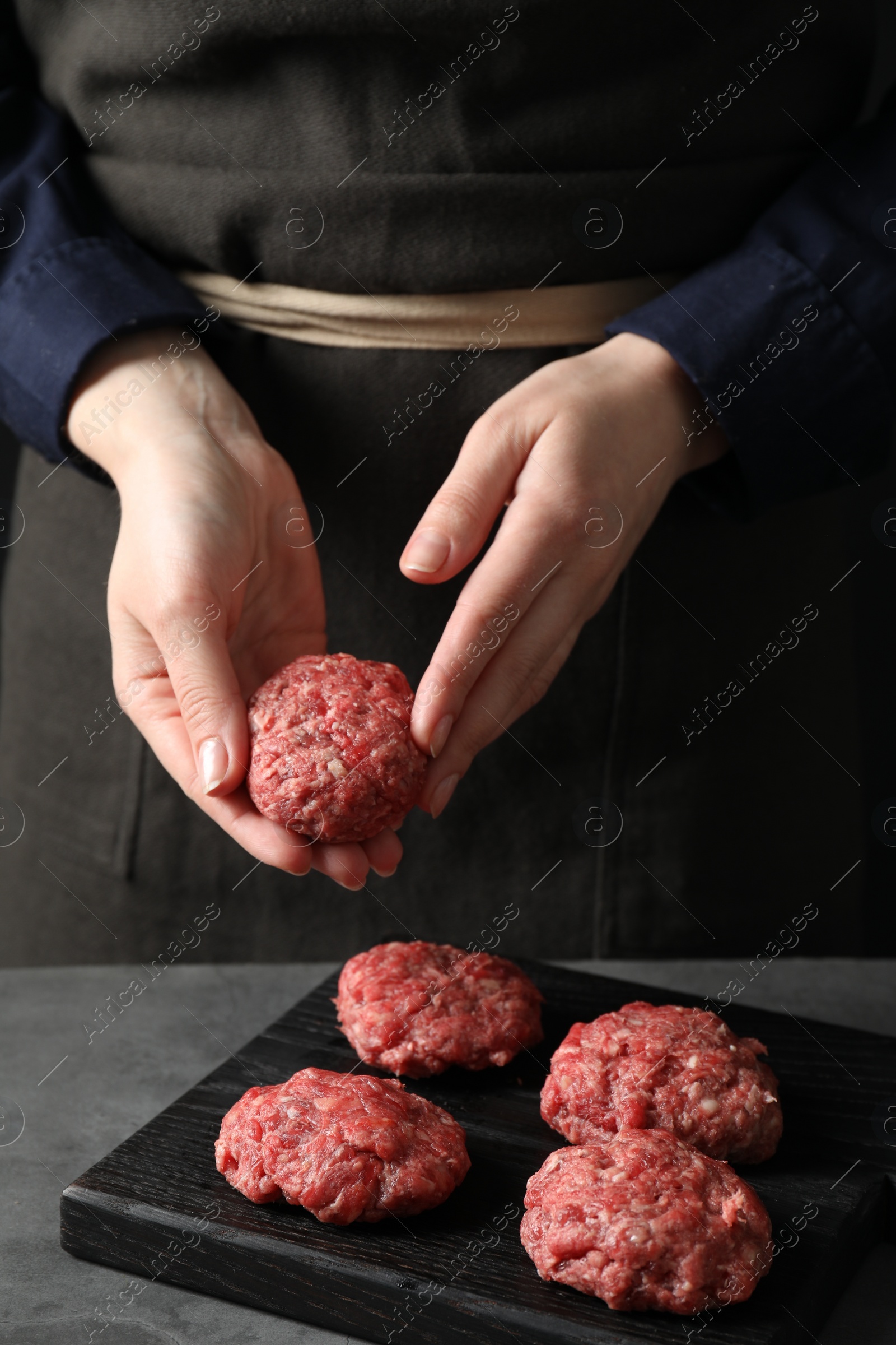 Photo of Woman making meatball from ground meat at grey table, closeup