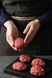 Woman making meatball from ground meat at grey table, closeup