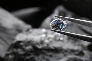 Tweezers with beautiful shiny diamond over stones, closeup. Space for text