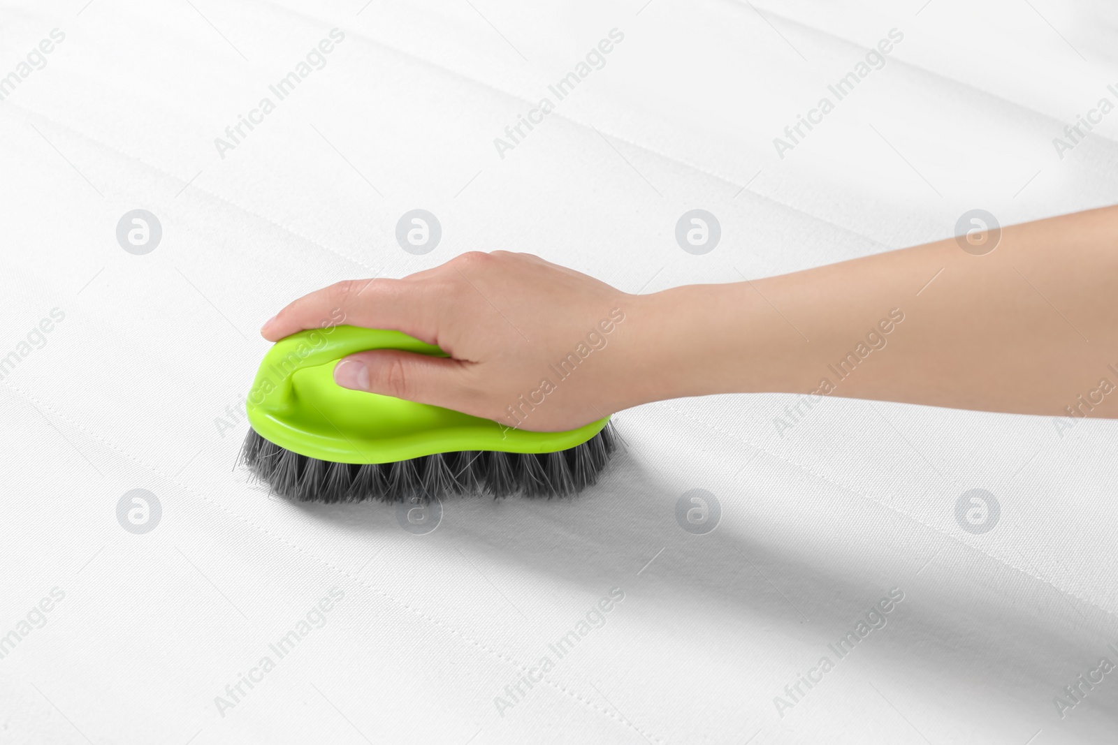 Photo of Woman cleaning white mattress with brush, closeup