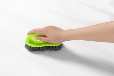 Photo of Woman cleaning white mattress with brush, closeup