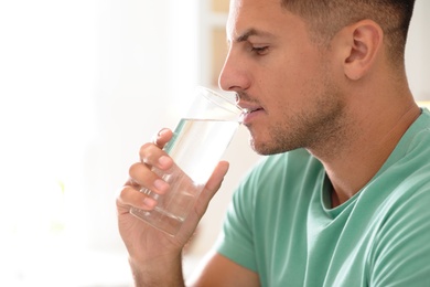 Photo of Man drinking pure water from glass indoors, closeup