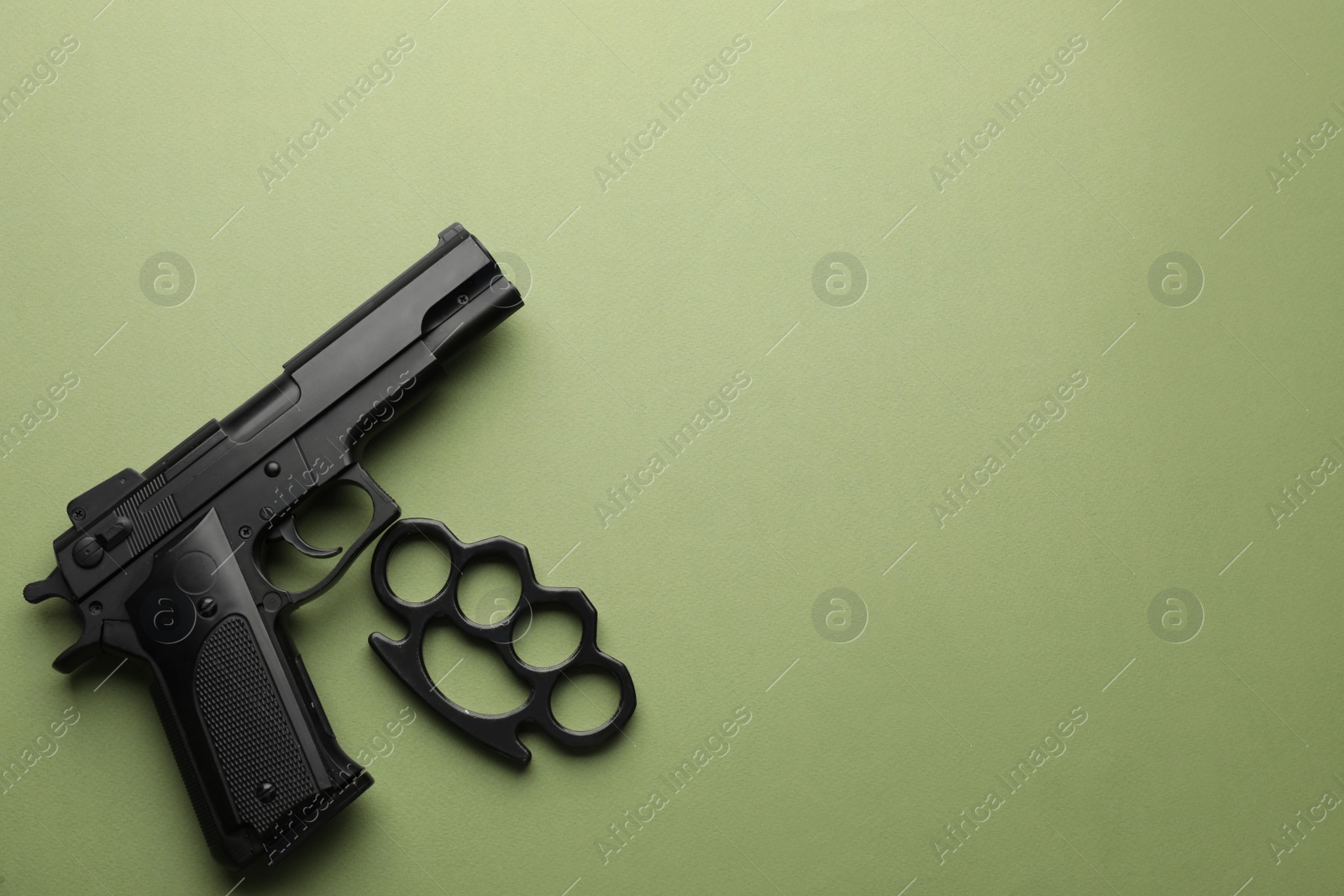 Photo of Black brass knuckles and gun on green background, flat lay. Space for text