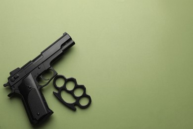 Photo of Black brass knuckles and gun on green background, flat lay. Space for text