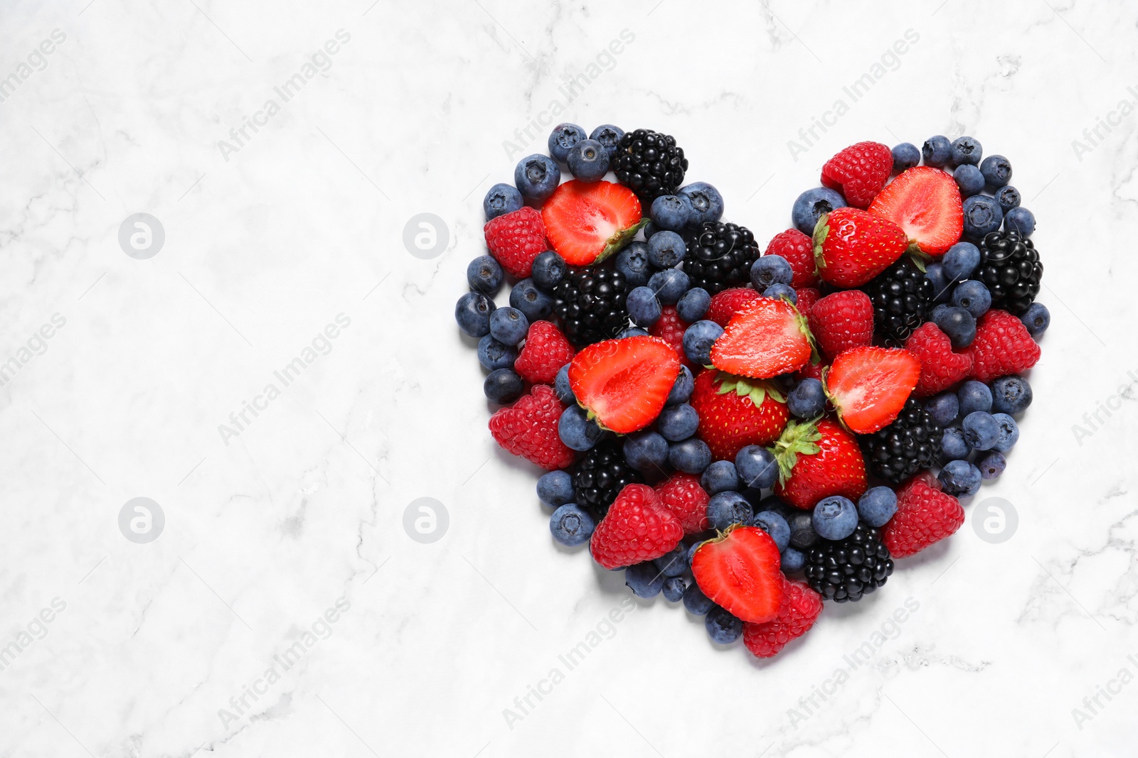 Photo of Heart made of different fresh ripe berries on white marble table, top view. Space for text