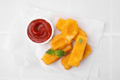 Photo of Tasty fried mozzarella sticks with basil leaves and ketchup on white tiled table, top view