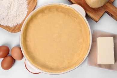 Photo of Pie tin with fresh dough and ingredients on white background, flat lay. Making quiche