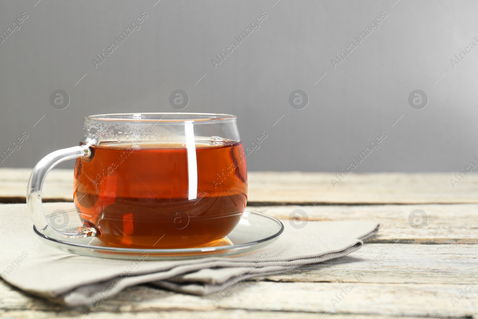 Photo of Aromatic tea in glass cup and napkin on wooden table. Space for text