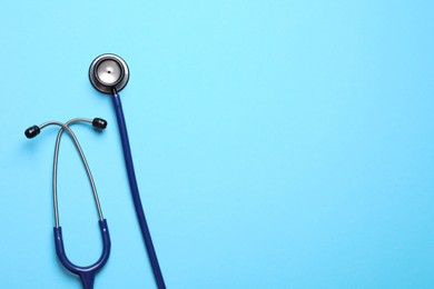 Stethoscope on light blue background, top view. Space for text