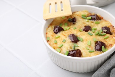 Photo of Tasty sausage casserole with green onions in baking dish served on white tiled table, closeup