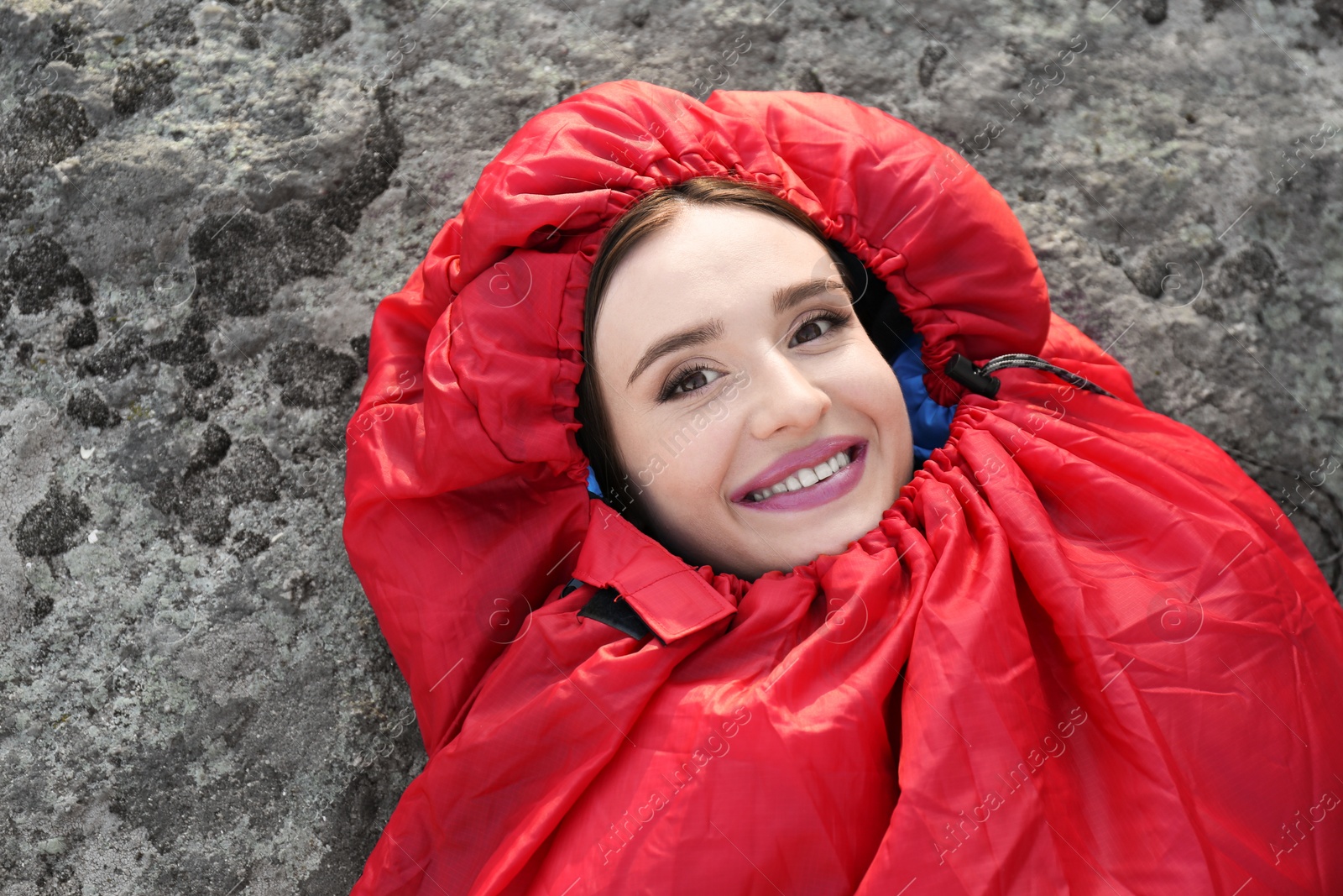 Photo of Young woman lying in red sleeping bag outdoors