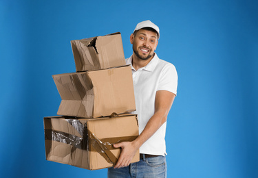 Photo of Emotional courier with damaged cardboard boxes on blue background. Poor quality delivery service