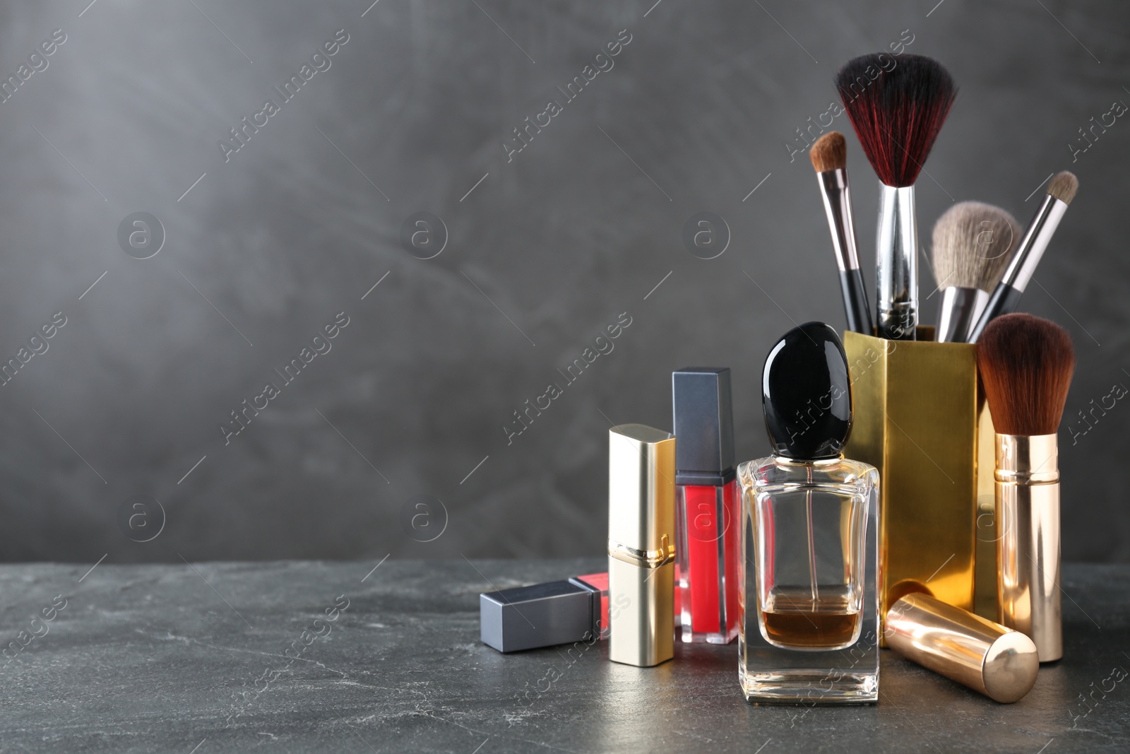 Photo of Bottle of perfume and makeup products on dark table, space for text