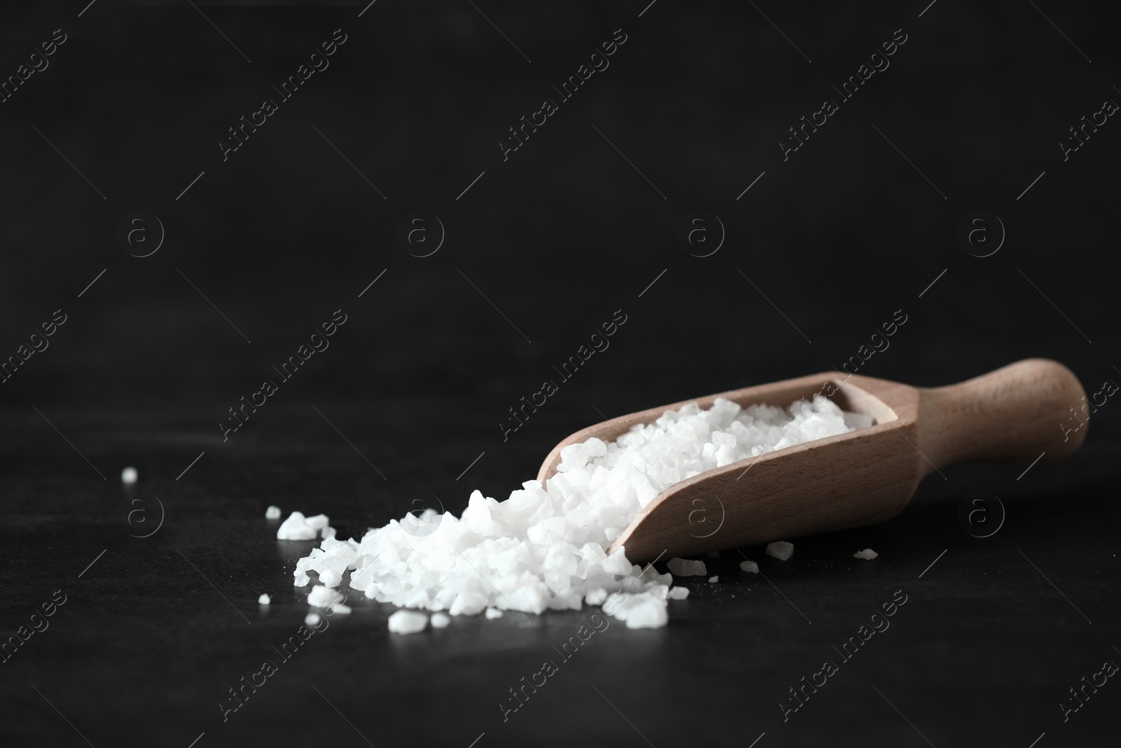 Photo of Organic salt and wooden scoop on black table. Space for text