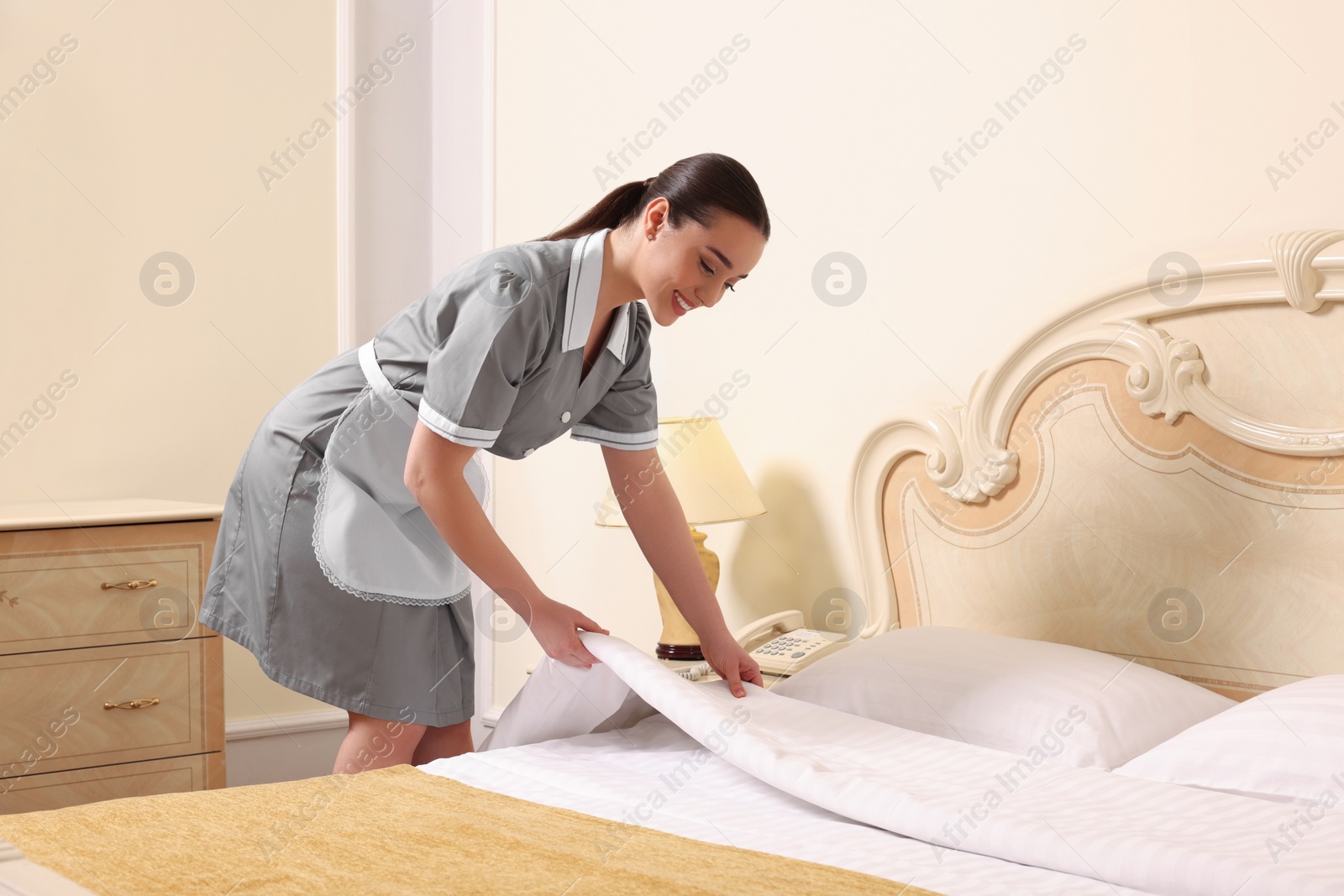 Photo of Young chambermaid making bed in hotel room. Space for text