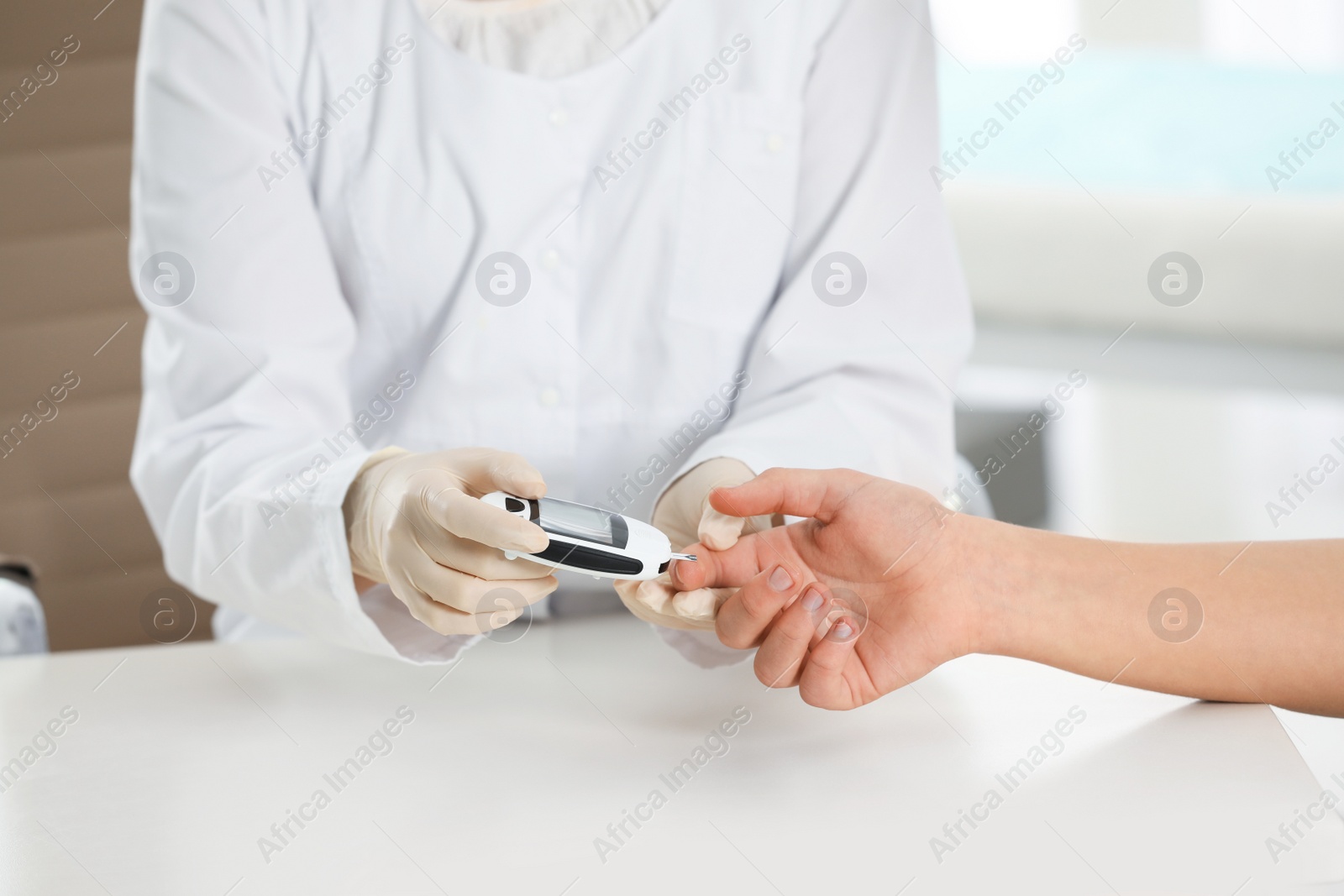 Photo of Doctor checking patient's blood sugar level with digital glucometer at table, closeup. Diabetes control