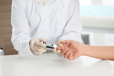 Photo of Doctor checking patient's blood sugar level with digital glucometer at table, closeup. Diabetes control