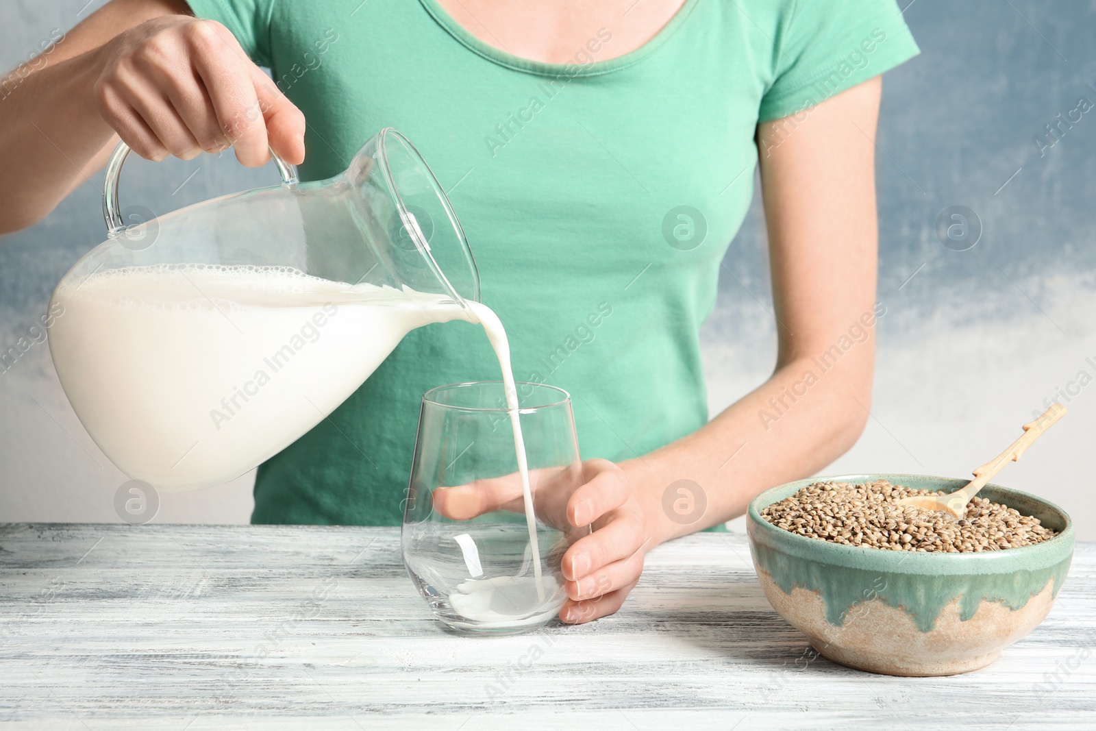 Photo of Woman pouring hemp milk into glass on table, closeup