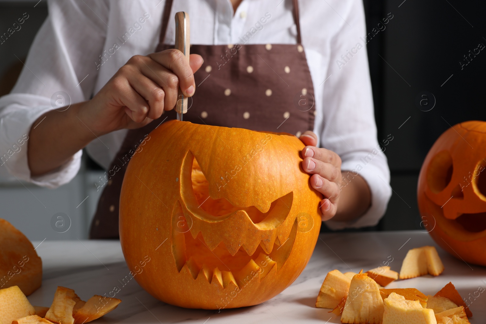 Photo of Woman carving pumpkin for Halloween at white marble table, closeup