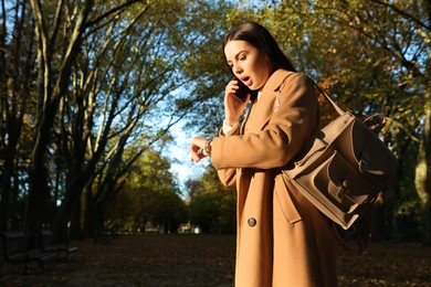 Emotional woman checking time while talking on smartphone in park. Being late concept