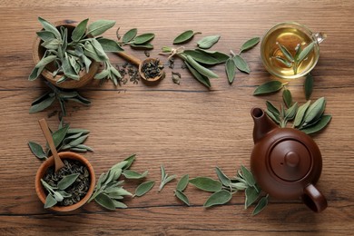 Photo of Flat lay composition with cup of sage tea, green leaves and teapot on wooden table. Space for text