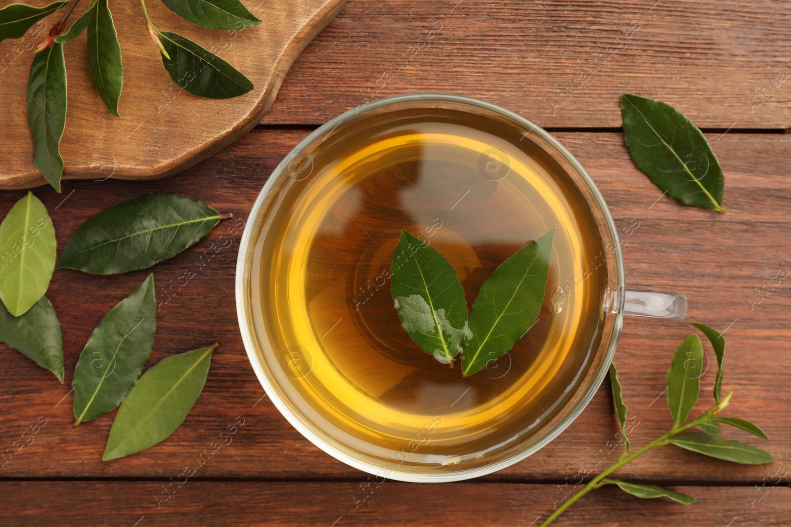 Photo of Cup of freshly brewed tea with bay leaves on wooden table, flat lay