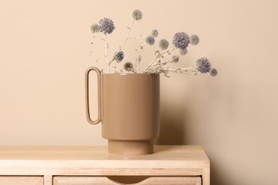 Stylish ceramic vase with wild flowers on wooden cabinet near beige wall