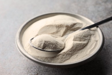 Photo of Bowl and spoon of agar-agar powder on grey table, closeup