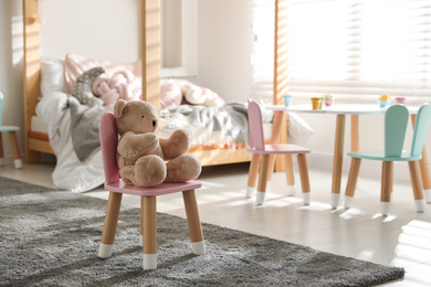 Photo of Cute chair with bunny ears and teddy bear in children's bedroom interior