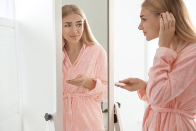 Young woman with eyelash loss problem looking in mirror indoors