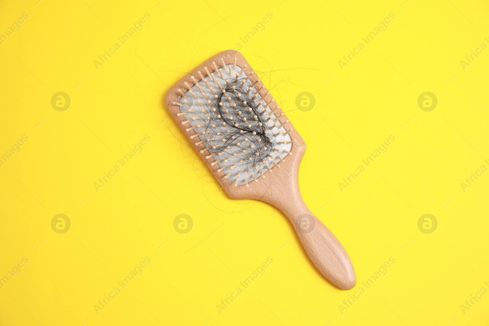 Photo of Wooden brush with lost hair on yellow background, top view