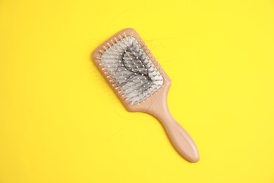Photo of Wooden brush with lost hair on yellow background, top view