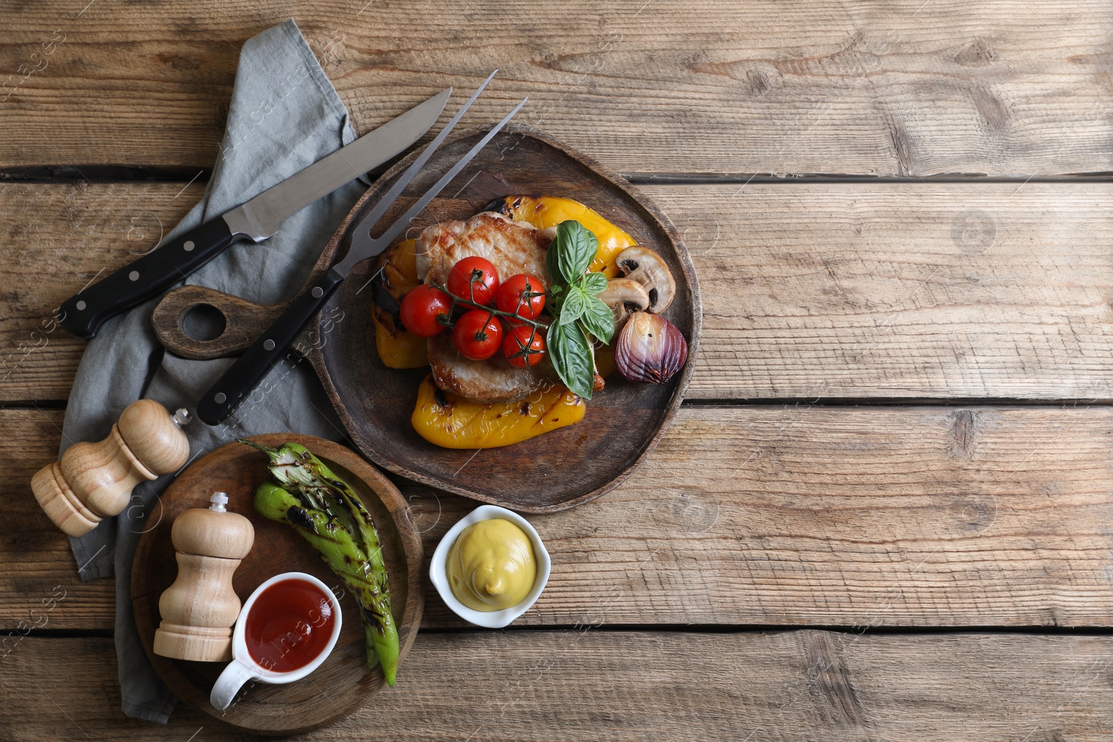 Photo of Delicious grilled meat and vegetables served with sauces on wooden table, flat lay. Space for text