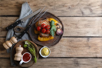 Delicious grilled meat and vegetables served with sauces on wooden table, flat lay. Space for text