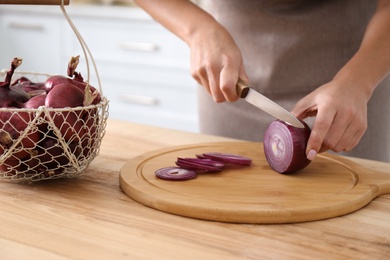Photo of Woman cutting red onion into rings at wooden table, closeup