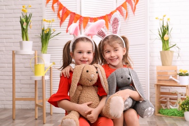 Photo of Adorable little girls with bunny ears and toy rabbits in Easter photo zone