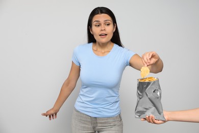 Beautiful young woman eating tasty potato chips on grey background