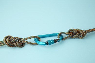 Photo of One metal carabiner with ropes on light blue background, space for text