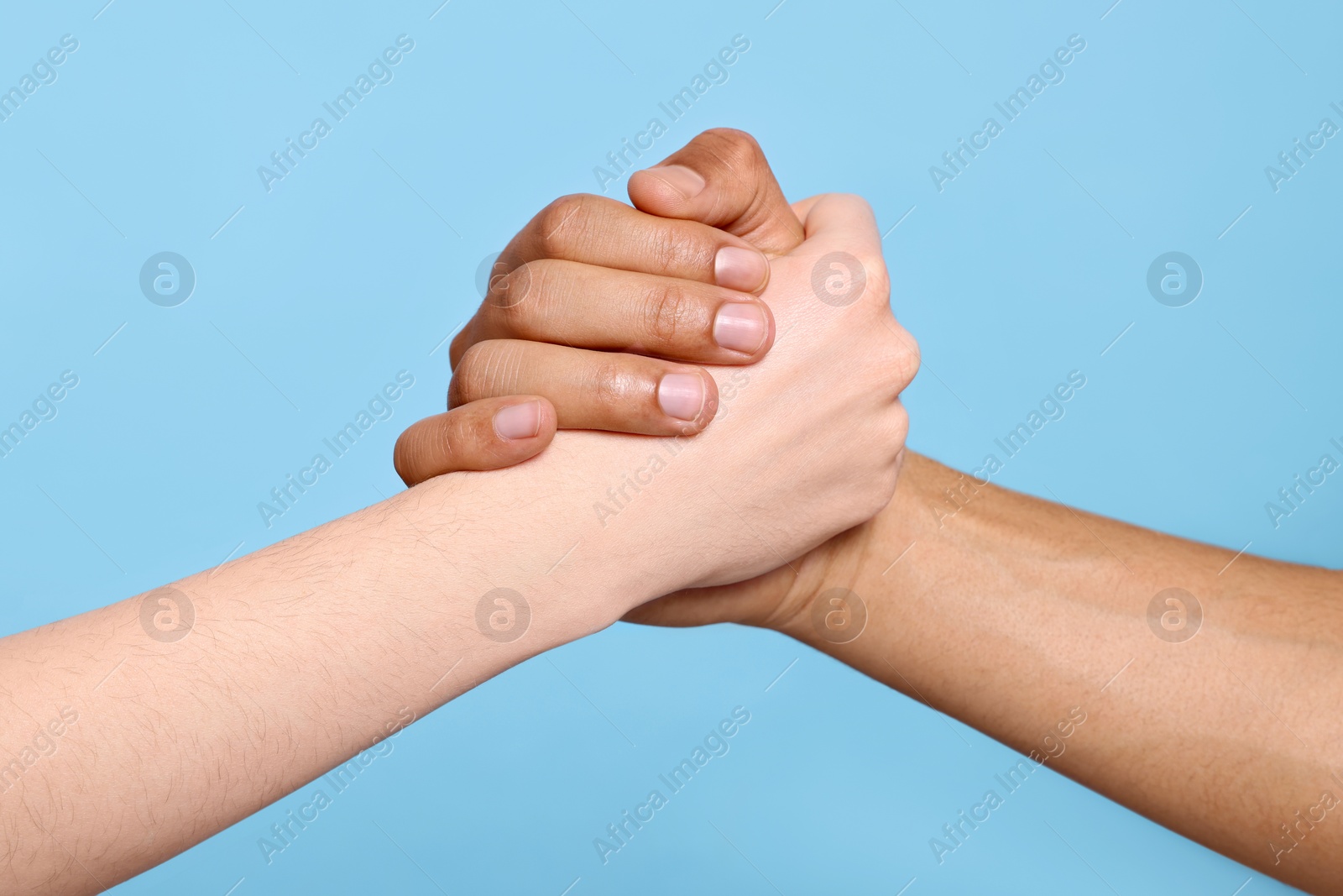 Photo of International relationships. People clasping hands on light blue background, closeup