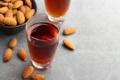 Glass with tasty amaretto liqueur and almonds on gray table, closeup. Space for text