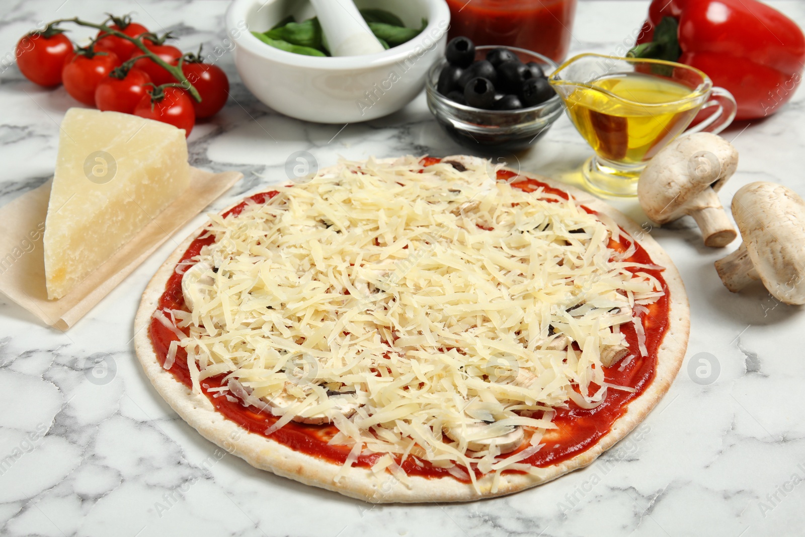 Photo of Unbaked pizza and ingredients on marble table