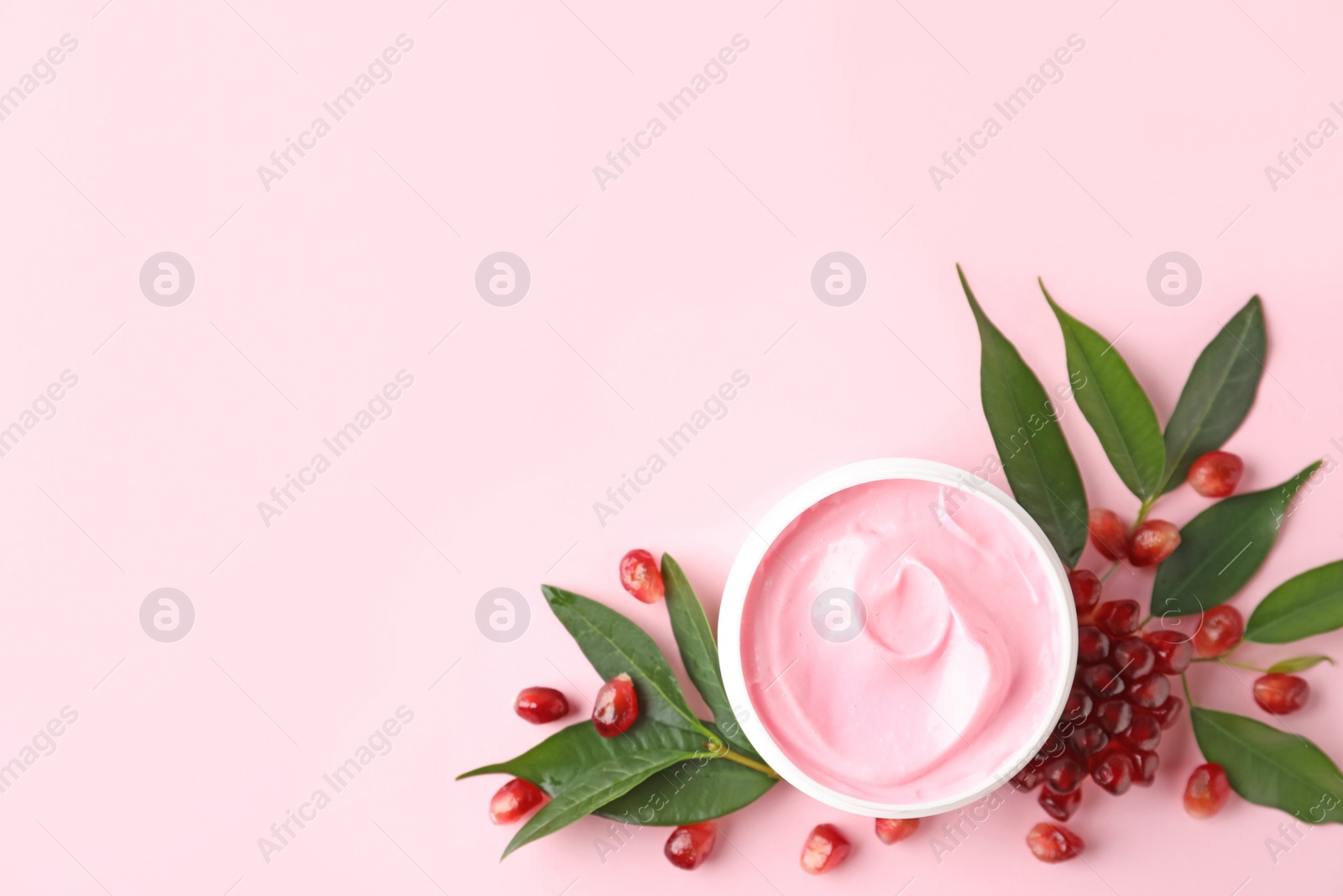 Photo of Fresh pomegranate and jar of facial mask on pink background, flat lay. Space for text