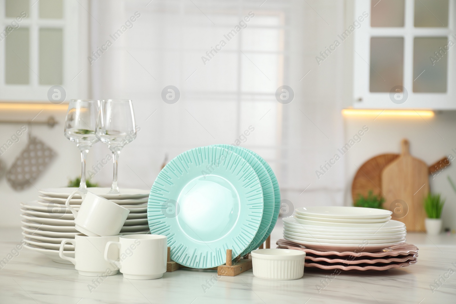 Photo of Clean plates, cups, glasses and bowl on white marble table in kitchen